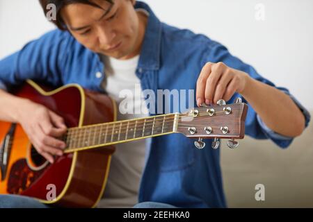 Japanese man playing guitar at home Stock Photo