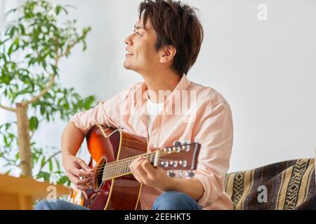 Japanese man playing guitar at home Stock Photo