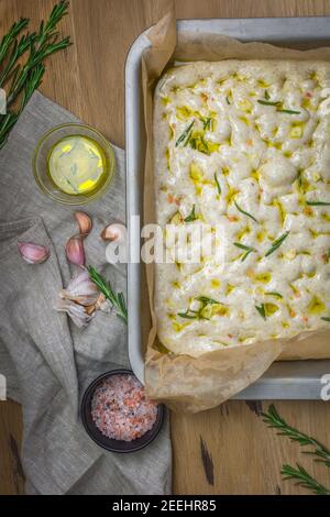 The process of making focaccia of natural sourdough with rosemary and garlic. Whole grain dough before baking on a wooden background. Artisan Stock Photo