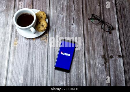 A mobile phone or cell phone laid on a wooden table with the Metro news app open on screen Stock Photo