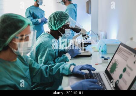 Multiracial medical scientists in hazmat suit working with microscope and laptop computer inside modern laboratory hospital - Focus african man face Stock Photo