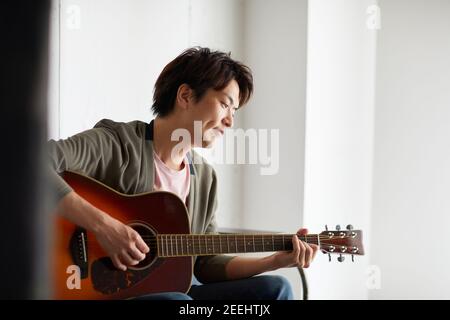 Japanese man playing guitar at home Stock Photo