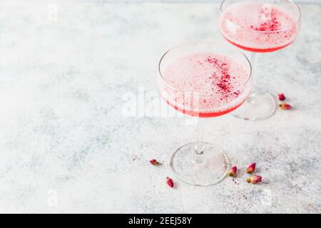 Pink alcoholic cocktail with lemonade, champagne or Martini in a champagne glass, with froth and decorated with dry rosebuds, cocktail like Daiquiri, Stock Photo