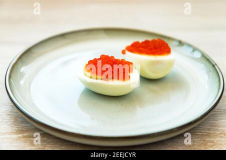 Red caviar stuffed halved eggs traditional Russian snack served on blue grey plate close up Stock Photo