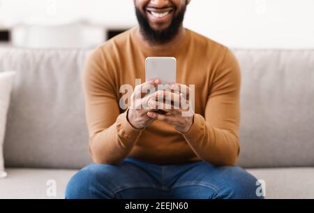 Unrecognizable African Man Using Smartphone At Home, Focus On Phone Stock Photo