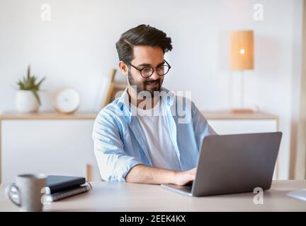 Smiling Arab Man Self-Entrepreneur Working With Laptop At Home Office Stock Photo