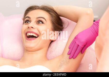 Young woman during armpit examination before waxing procedure laughing in a beauty salon Stock Photo