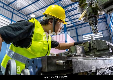 Asian machinist in safety suit operating the professional lathes in metalworking factory, lathe grinding metalworking industry concept Stock Photo