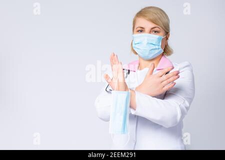 Doctor in protective mask showing stop gesture on gray background. Prevent spreading of coronavirus. Female doctor hands showing crossed stop sign Stock Photo