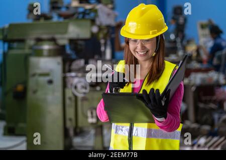 Portrait of Asian woman sales engineer checking the job list in paper over the photo blurred of lathe and milling machine background in metal factory, Stock Photo