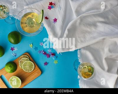 glasses of wine and spirits on white crumpled cloth with blue background, table with cut lime slices and remnants Stock Photo