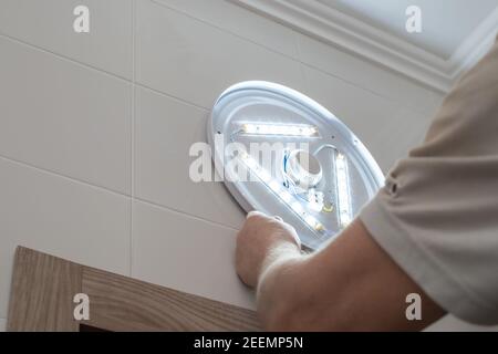 A man installs an LED lamp in the bathroom. Repair and improvement of housing. Stock Photo