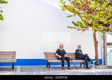 October 7, 2020 - Barbacena, Portugal: Elderly couple sitting and resting on the bench on the public square Stock Photo