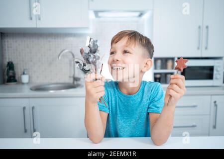 happy kid boy hold handmade sweets or candies on stick in hands at home kitchen Stock Photo