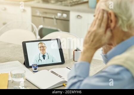 Cropped photo of smiley healthcare professional appearing on tablet screen while having online consultation with eldelry patient Stock Photo