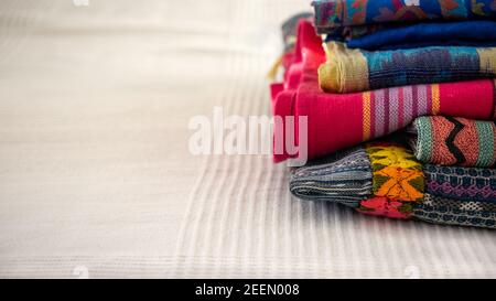 Piled multicolored vibrant ethnic hand woven textiles made in Southern America on a white cloth background. Fair trade concept. Close up. Stock Photo