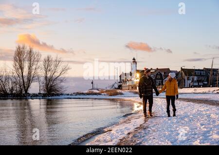 Urk Netherlands lighthouse during winter with snow covered coastline, Urk view at the lighthouse snowy landscape winter weather in Holland. Europe, couple watching sunset at the snow covered beach
