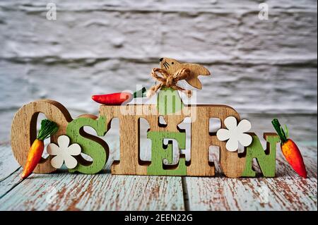 Wooden sign with an Easter bunny with carrots as decoration. The Text is German for Easter. Stock Photo