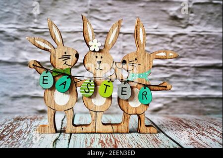 Three wooden Easter bunnies with decoration and the text Easter written on eggs. Stock Photo