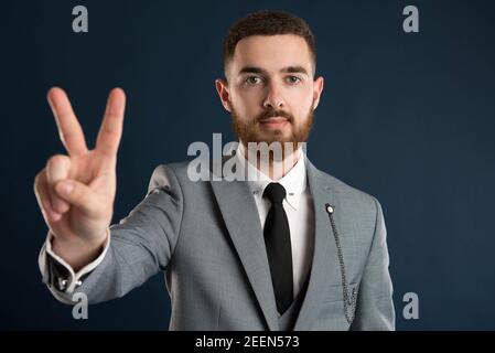 Young businessman showing peace sign wearing a grey suit Stock Photo