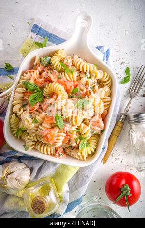 Spring diet healthy vegan pasta. Italian fusilli pasta with tomatoes, green vegetables, fresh herbs, cream cheese or feta, on white table background c Stock Photo