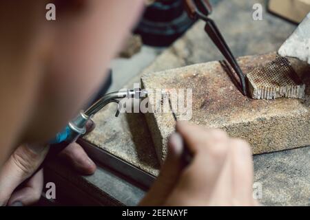 Diligent jeweler working on a chain heating up some links Stock Photo