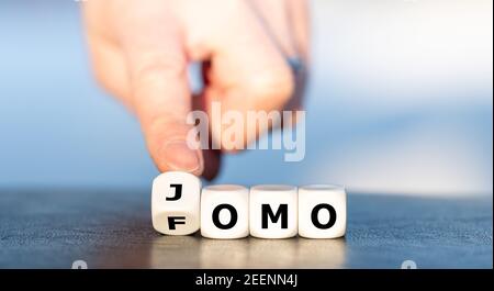 Hand turns dice and changes the abbreviation FOMO (fear of missing out) to JOMO (joy of missing out). Stock Photo
