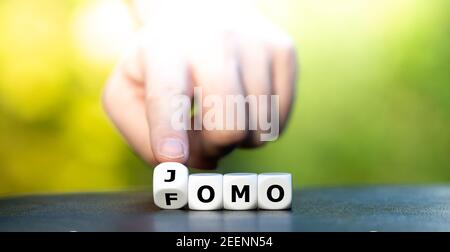 Hand turns dice and changes the abbreviation FOMO (fear of missing out) to JOMO (joy of missing out). Stock Photo