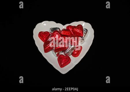 Foil Covered Chocolate Hearts on White Plate on Black Background Stock Photo