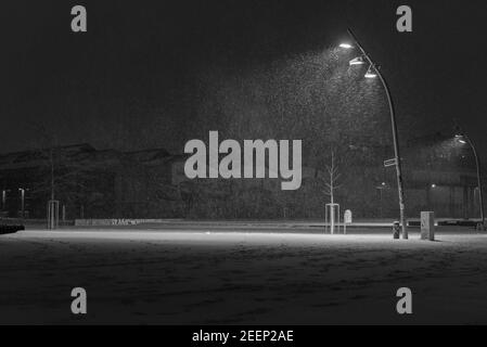 Snow flurries on a square in the evening, street lights and snow flurries, it snows in the evening on a large, illuminated square, black and white Stock Photo