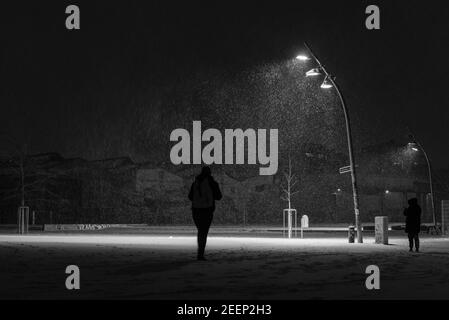 Snow flurries on a square in the evening, street lights and snow flurries, it snows in the evening on a large, illuminated square, one person Stock Photo