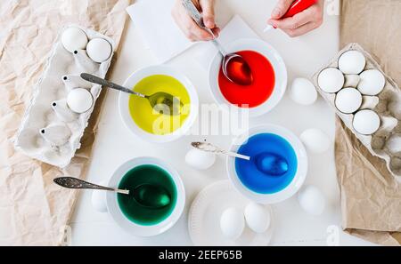 Flat lay. Dyeing Easter eggs with liquid food coloring. Different colors in different bowls Stock Photo