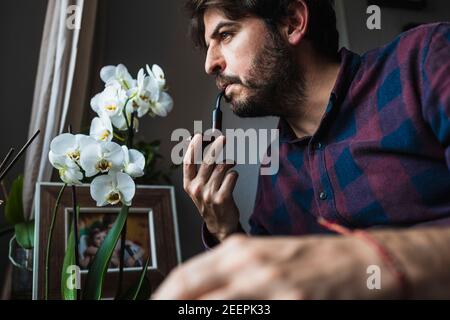 A man in his 40s looks out of a window smoking a pipe. Concept of bein Stock Photo