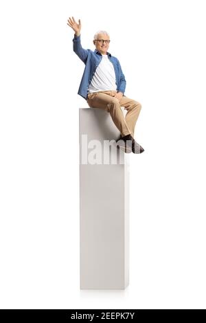 Smiling mature man sitting on a column and waving at camera isolated on white background Stock Photo