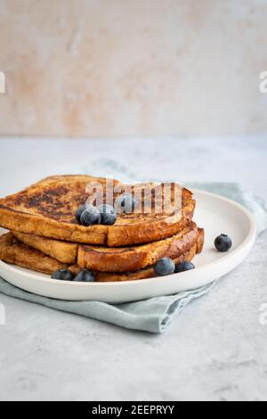 Side view of three slices of french toast with blueberries on a plate on grey background, minimalistic style with copy space Stock Photo