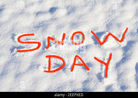 SNOW DAY written in bright red capital letters in fresh snowfall signifies No School and school closure due to dangerous weather conditions. Stock Photo