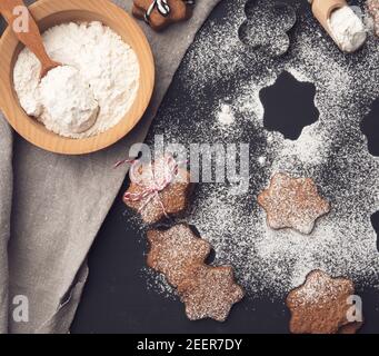 baked star-shaped gingerbread cookie sprinkled with powdered sugar on a black table and ingredients Stock Photo