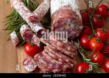 Sliced Air-dried salami with rosemary and cherry tomatoes - wood background Stock Photo