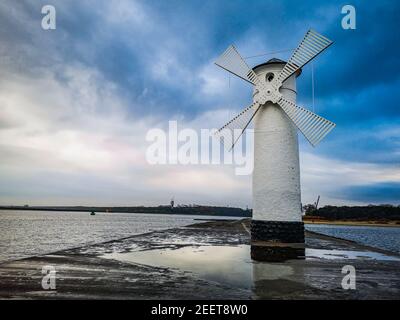 White Windmill at end of coast full of puddles near Baltic sea in Swinoujscie Stock Photo