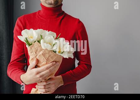 Man in red sweater holding a bouquet of white tulis. Stock Photo