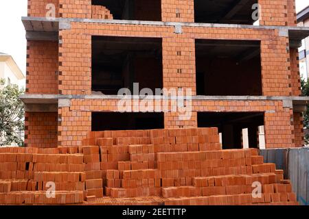 Clay brick building material and building under construction in the background. Stock Photo