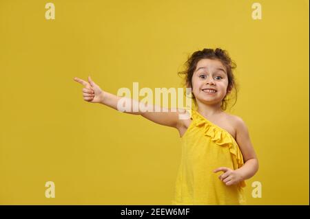Adorable little baby girl points his finger right to the yellow background with copy space Stock Photo
