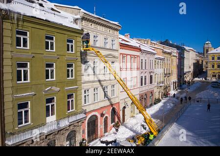 Lviv, Ukraine - February 16, 2021: Workers remove icicles from building roofs on Market square in Lviv. View from drone Stock Photo