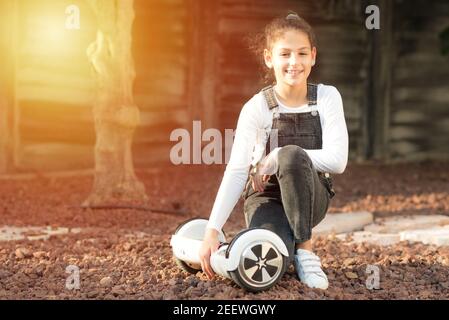 Beautiful kid Smile with Braces.Young hipster teenager girl sit with electric Hover Board, Dual Wheel Self Balancing Electric Skateboard at the sunny park, child using two-wheeled board. Copy space. Stock Photo