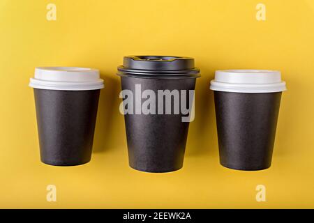 Three disposable paper black cups different sizes with close plastic lids for takeout coffee, which is then recyclable. Take away drink. Empty mock up Stock Photo