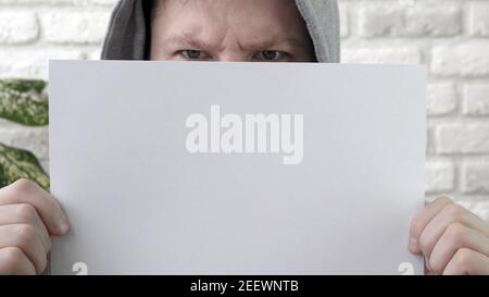 A man with an empty sheet of paper for a text set, a poster for a text, a man with a frown with a copy space poster Stock Photo