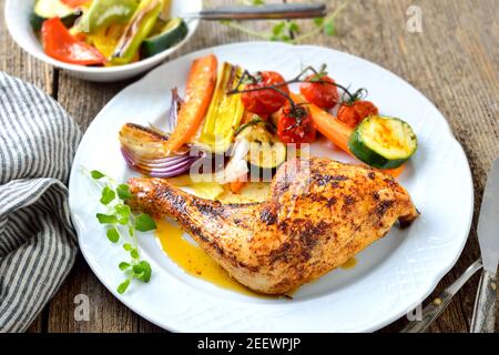 Crispy oven roasted chicken leg with colorful mediterranean vegetables hot served on a white plate Stock Photo