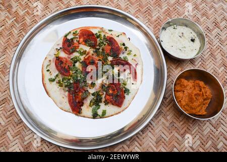 South indian food Uttapam also known as Uttapa is an Indian savoury pancake. Topping of sliced tomato, coriander and onion. This is Tomato uttapam wit Stock Photo