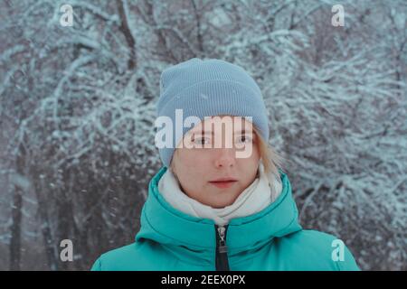 Portrait of a beautiful teenage girl 15 years old with brown eyes. Background of tree branches in hoarfrost and snowfall. Stock Photo