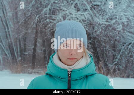 Teenager girl in park in winter looks to side. Background of beautiful tree branches in hoarfrost and snowfall. Stock Photo